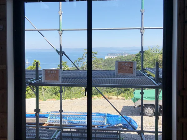 白浜の別荘：施工中の窓から足場越しに望む、青空と海