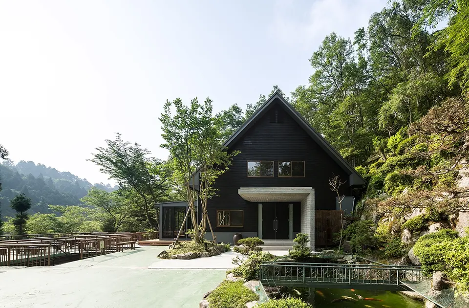 亀岡のVILLA／保養所。池と植栽のある庭から、切妻屋根の正面と玄関ポーチを望む
