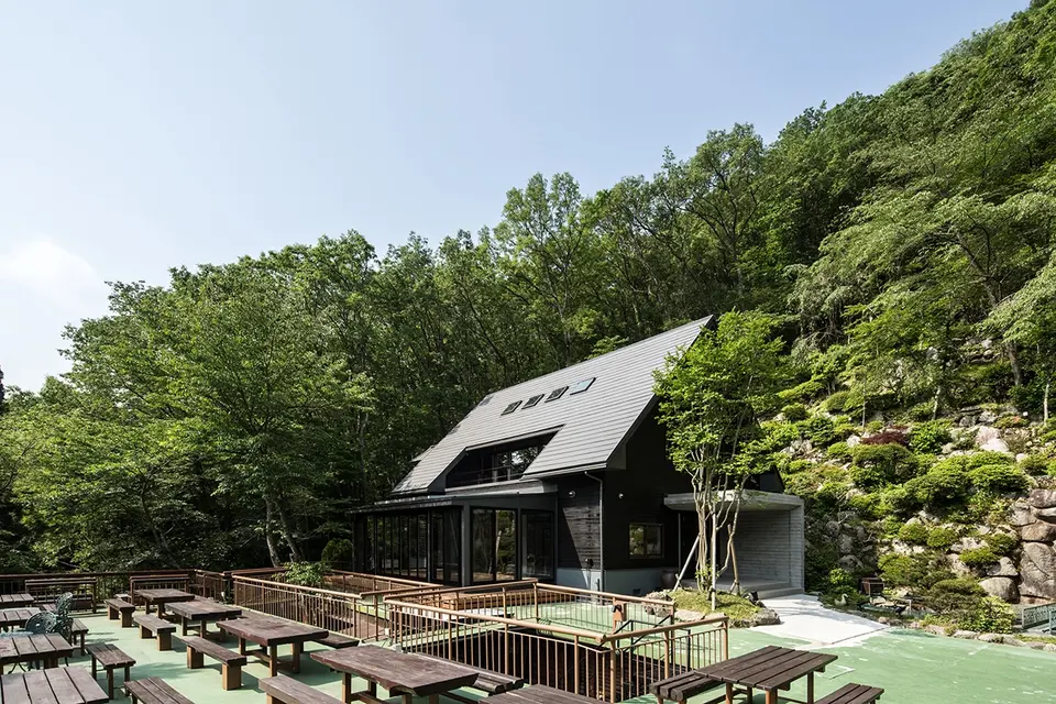 亀岡のVILLA／保養所。天窓のある大屋根とガラス張りのサンルーム、屋外テーブルが並ぶテラスを望む