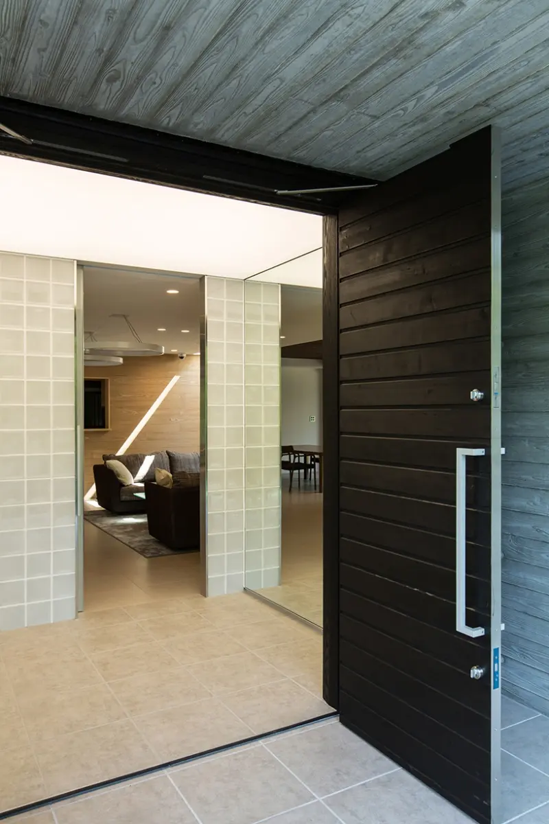 亀岡のVILLA／保養所。開いた木製の玄関扉から、ガラスブロックの壁と奥のソファスペースを望む
