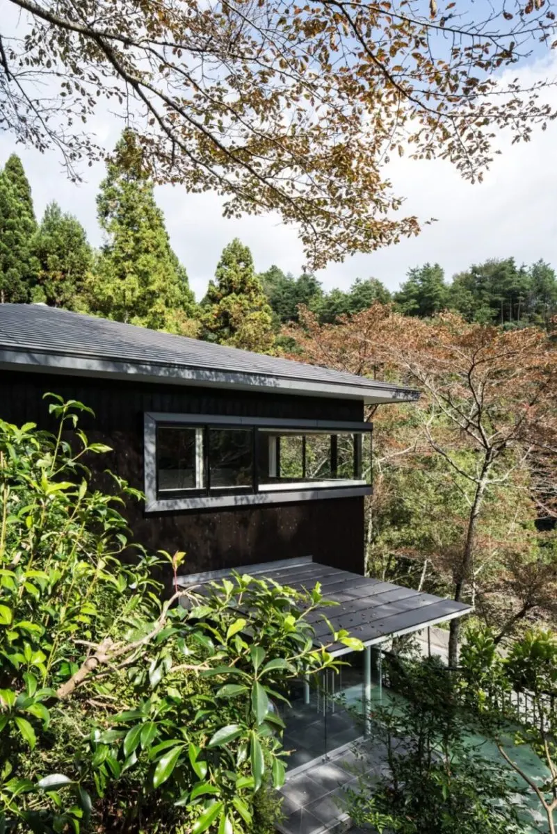 亀岡のVILLA／保養所。木々の間から望む黒い外壁と横長窓、庇を設けた玄関
