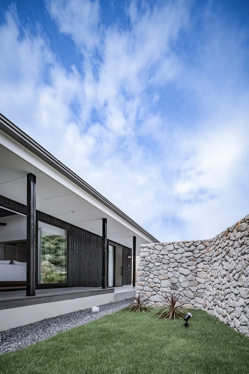 上芳養のコートハウス。石塀に囲まれた芝生の中庭から、黒い外壁と深い軒のある建物を見上げる