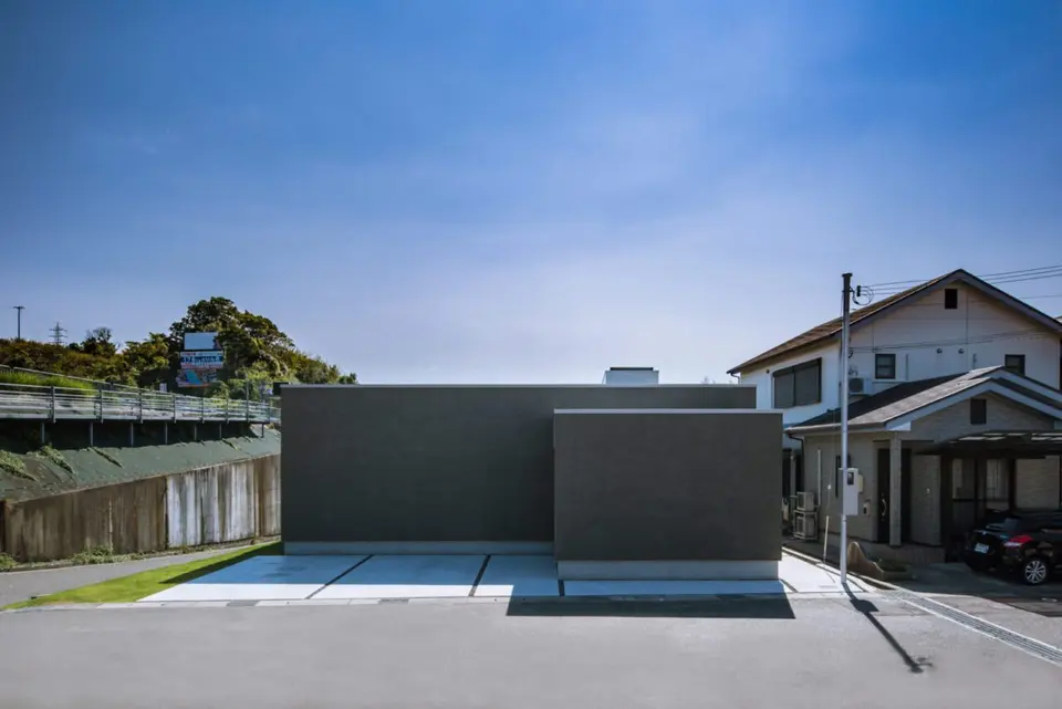 新庄のスクエアコートハウス。道路側に窓を設けないグレーの外壁と、建物前の駐車スペース。
