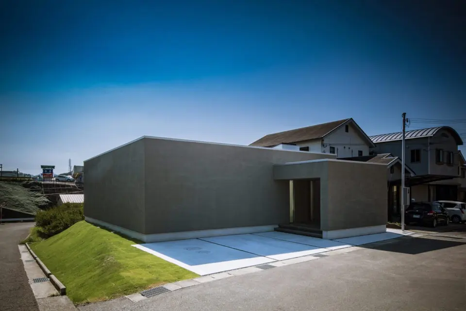 新庄のスクエアコートハウス。芝生の斜面に沿って建つ平屋。外壁の一角をくぼませた玄関アプローチ。