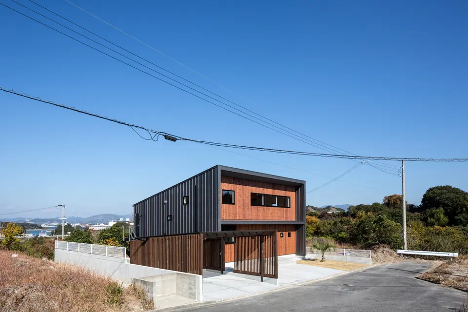 新庄のスキップハウス。金属と木張りの外壁を組み合わせた建物とカーポートを、周辺の風景とともに望む